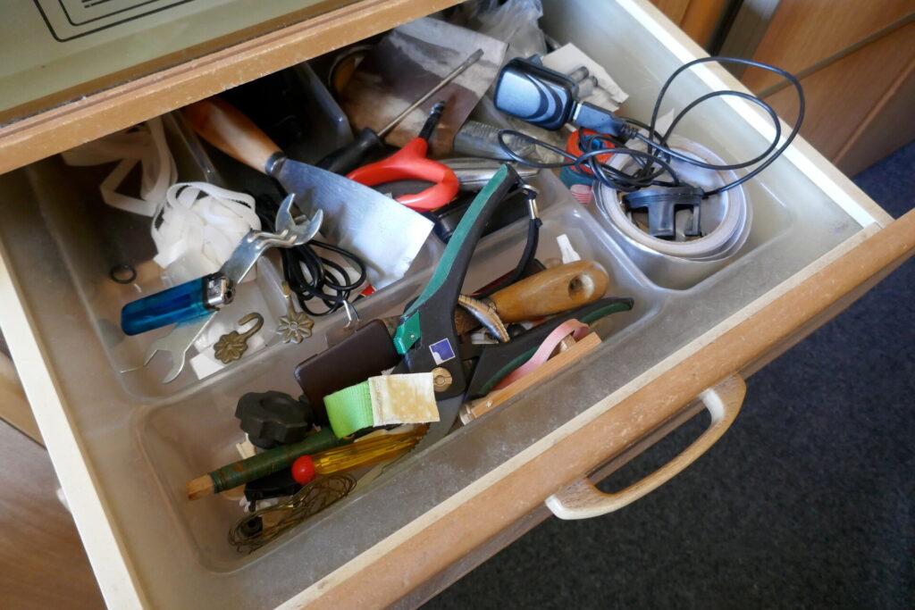 Blick in eine unordentliche Schublade, gefüllt mit Werkzeugen, Haushaltsgegenständen und verschiedenen anderen Gegenständen.
