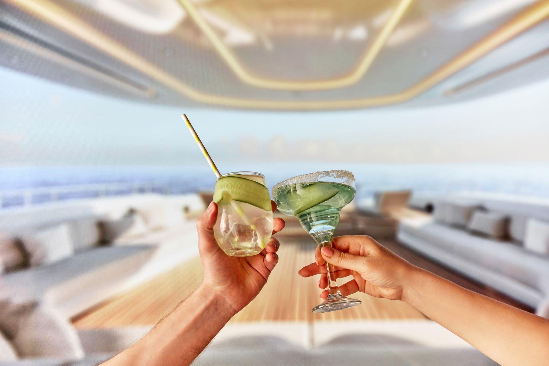 Tropische Luxusreisen. Fokus auf männliche und weibliche Hände, die erfrischende Cocktails mit Gurkenscheiben halten. Genießen Sie Getränke auf luxuriösen Yacht. Sommer, Urlaub, Reisen, Entspannung, Natur Konzept