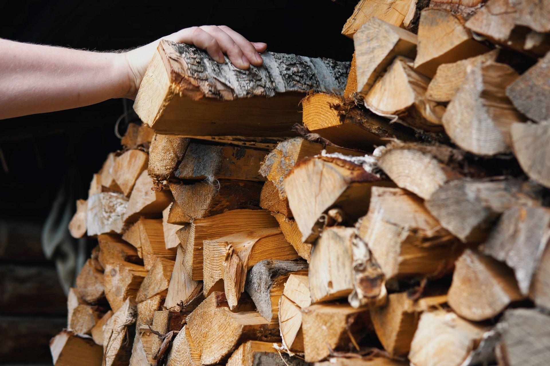 Hand stapelt trockenes Brennholz im Schuppen