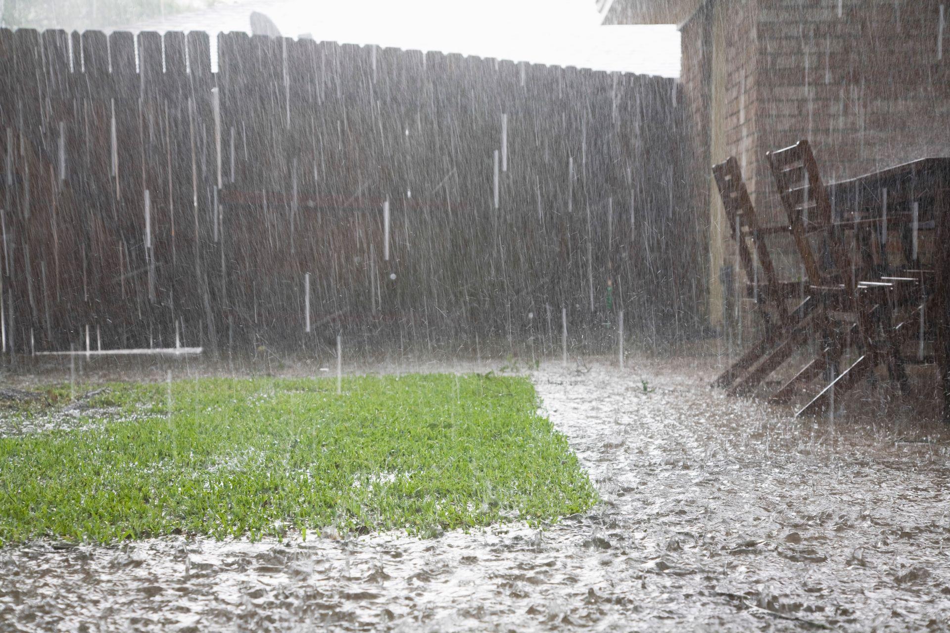Starker Regen auf Terrasse mit Garten und Holzzaun zeigt Bedarf an Doppelstegplatten-Wetterschutz.